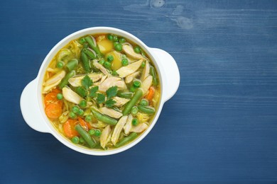 Saucepan of delicious vegetable soup with chicken on blue wooden table, top view. Space for text