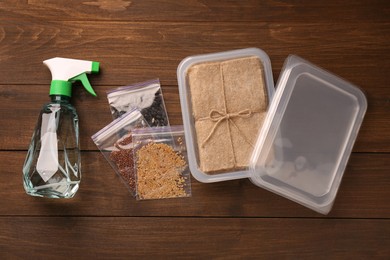 Microgreens growing kit. Different seeds, mats, containers and spray bottle on wooden table, flat lay