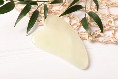 Jade gua sha tool and branches on white wooden table, closeup