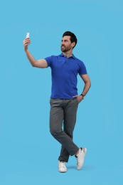 Photo of Smiling man taking selfie with smartphone on light blue background