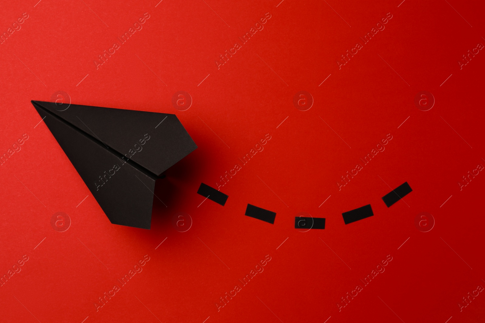 Photo of Handmade black paper plane with dotted lines on red background, top view