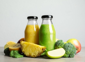 Photo of Bottles of delicious juices and fresh fruits on grey table