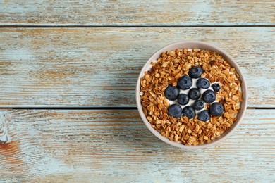 Photo of Bowl of yogurt with granola and blueberries on old wooden table, top view. Space for text