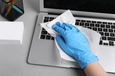 Woman wiping laptop with paper towel at gray table, closeup