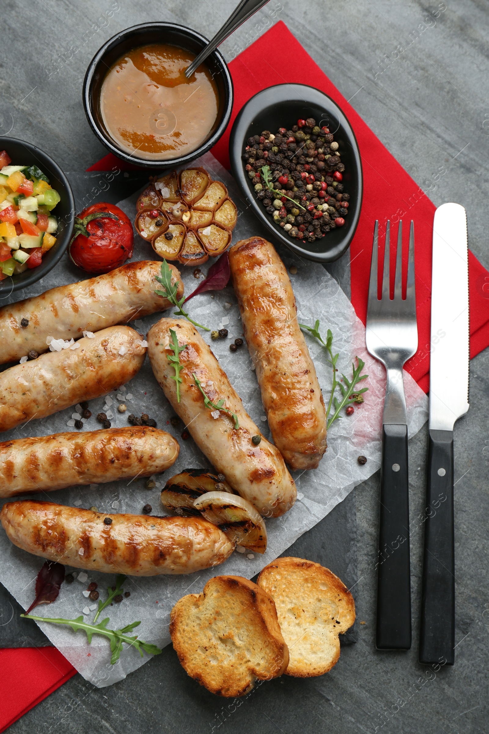 Photo of Tasty fresh grilled sausages served with vegetables on grey table, flat lay