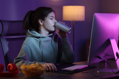 Girl with energy drink playing computer game at table in room