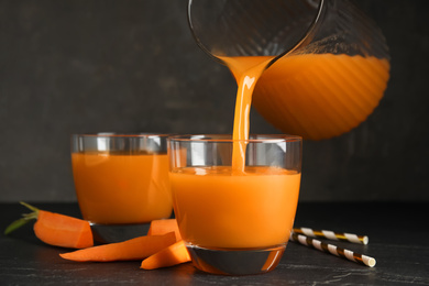 Photo of Pouring freshly made carrot juice into glass on black table