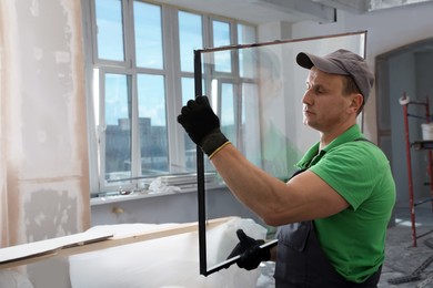 Worker in uniform holding double glazing window indoors