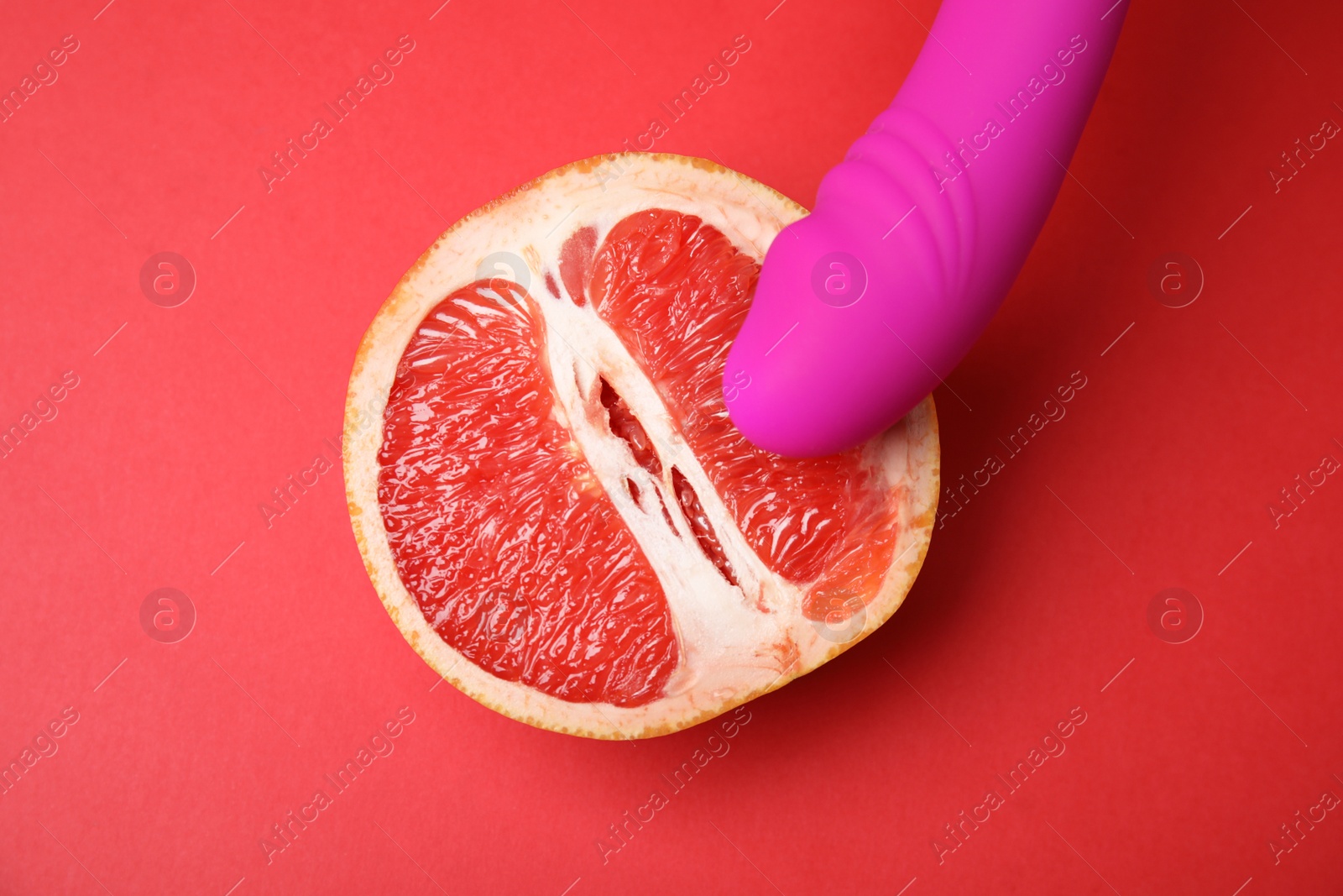 Photo of Half of grapefruit and purple vibrator on red background, flat lay. Sex concept