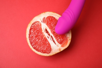 Half of grapefruit and purple vibrator on red background, flat lay. Sex concept