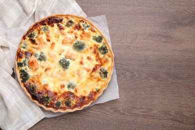 Photo of Delicious homemade quiche with salmon and broccoli on wooden table, top view. Space for text