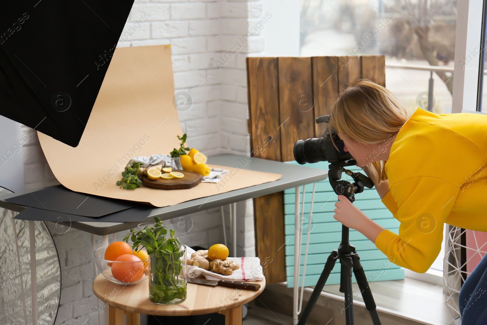 Photo of Young woman taking picture of lemons, mint and ginger in professional studio. Food photography
