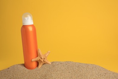 Photo of Sand with bottle of sunscreen and starfish against orange background, space for text. Sun protection
