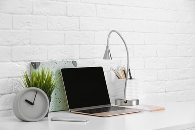 Modern workplace with laptop on table against brick wall. Mockup for design