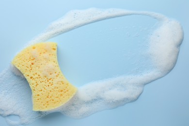 Photo of Yellow sponge with foam on light blue background, top view. Space for text