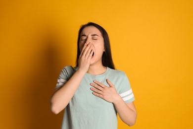 Photo of Young tired woman yawning on yellow background