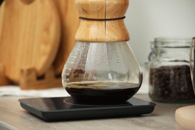 Photo of Glass chemex coffeemaker with coffee and scales on table, closeup