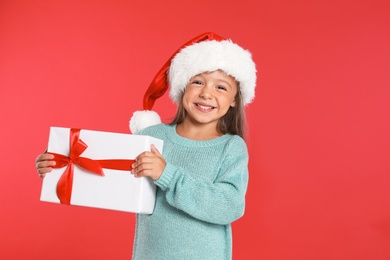 Happy little child in Santa hat with gift box on red background. Christmas celebration