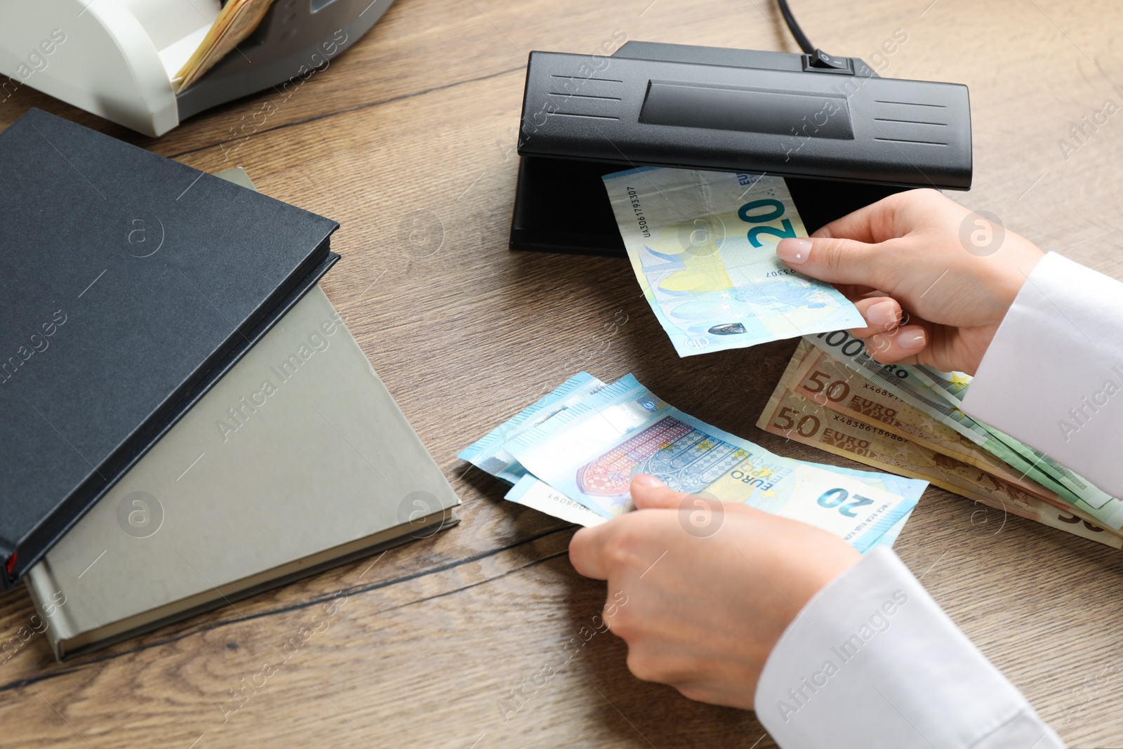 Photo of Woman checking Euro banknotes with currency detector at wooden table, closeup. Money examination device