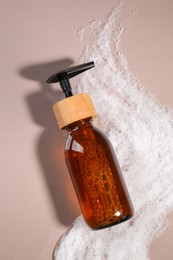Photo of Bottle of cosmetic product and foam on brown background, top view