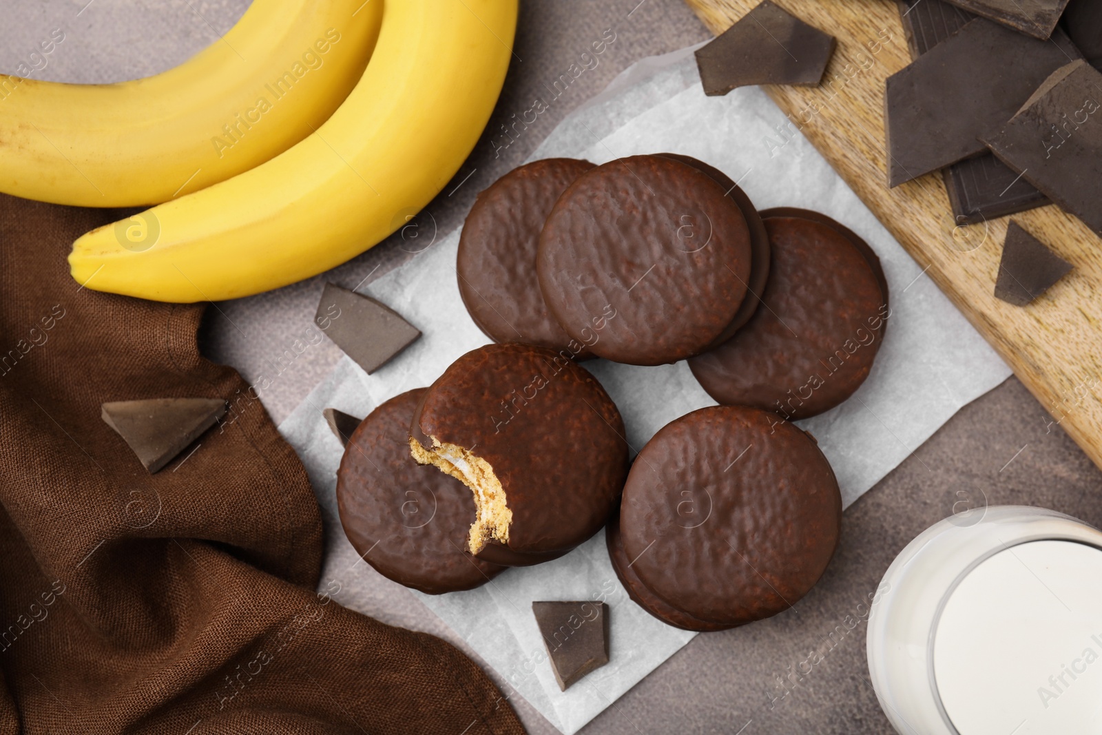 Photo of Tasty banana choco pies, pieces of chocolate and fruits on textured table, flat lay