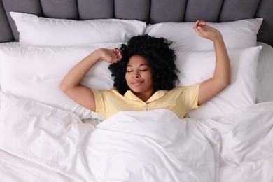 Photo of Beautiful young woman stretching in soft bed, above view