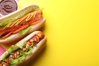 Photo of Delicious hot dogs with lettuce and sauces on yellow background, flat lay. Space for text