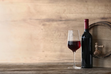 Glass and bottle of red wine near wooden barrel on table. Space for text