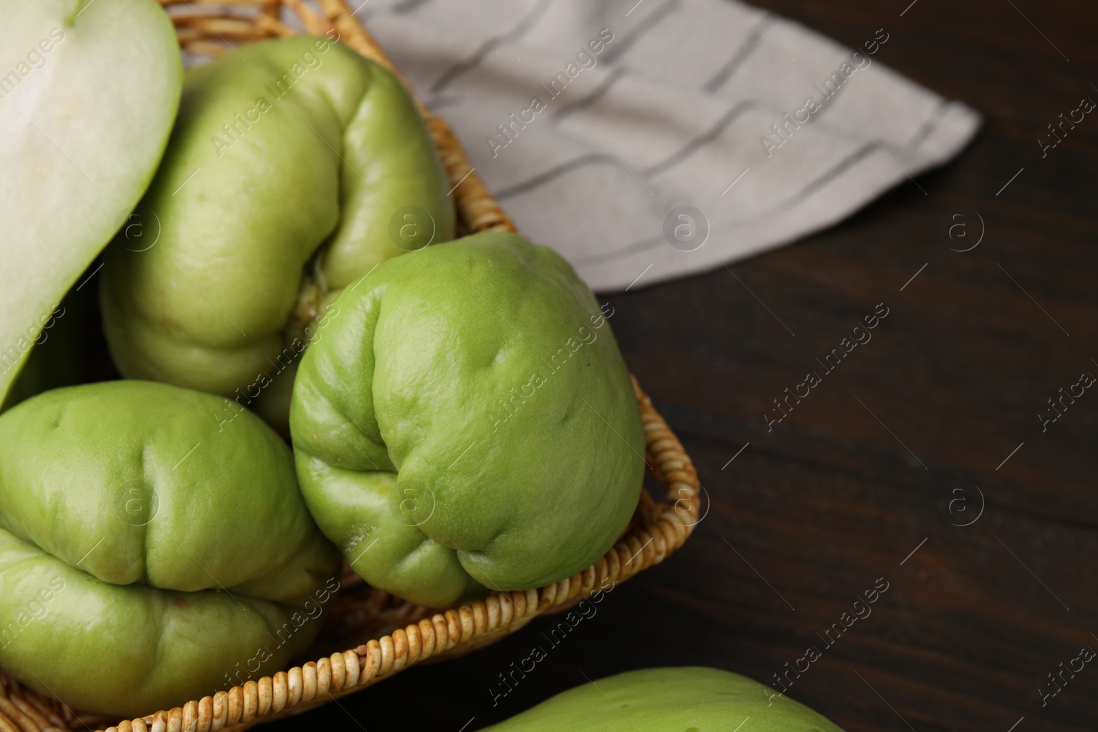 Photo of Fresh green chayote in wicker basket on wooden table, closeup