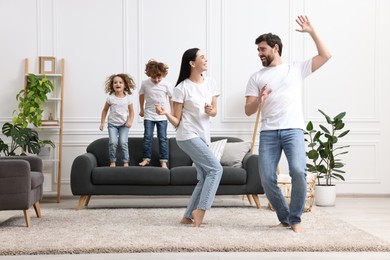 Photo of Happy family having fun in living room. Couple dancing while children jumping on sofa