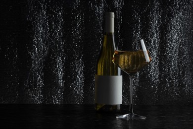 Photo of White wine in glass and bottle on black table, space for text