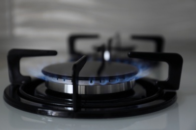 Photo of Gas burner with blue flame on modern stove, closeup