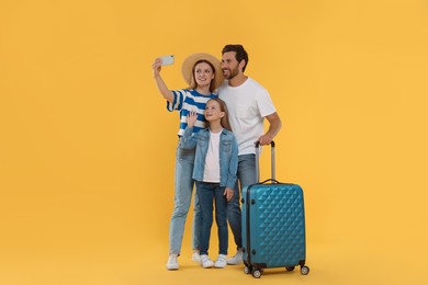 Photo of Happy family with suitcase taking selfie on orange background