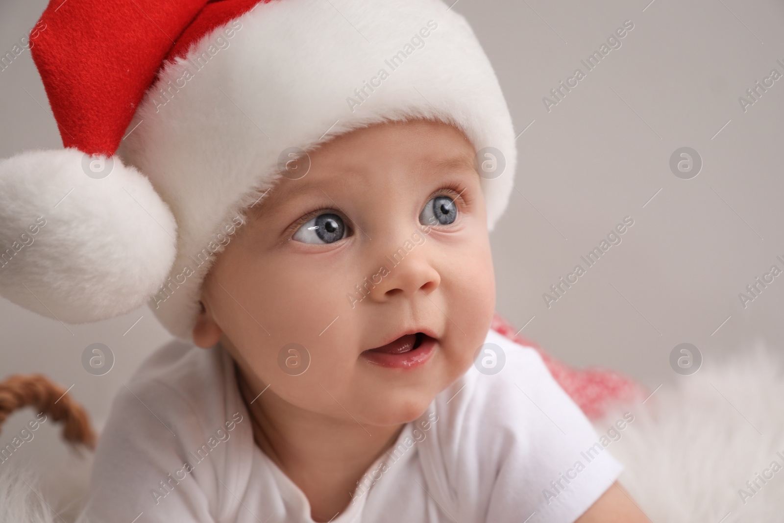 Photo of Cute baby in Santa hat on light grey background, closeup. Christmas celebration