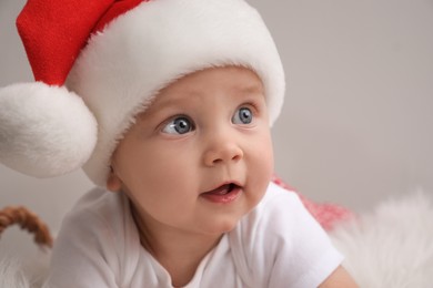 Cute baby in Santa hat on light grey background, closeup. Christmas celebration