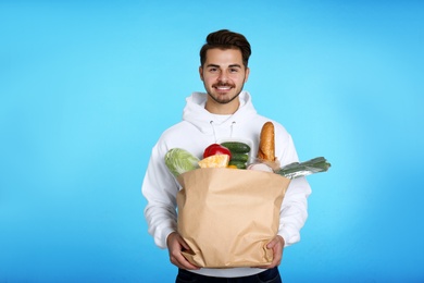 Photo of Young man holding paper bag with products on color background. Food delivery service