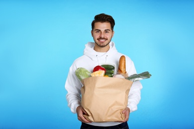 Young man holding paper bag with products on color background. Food delivery service