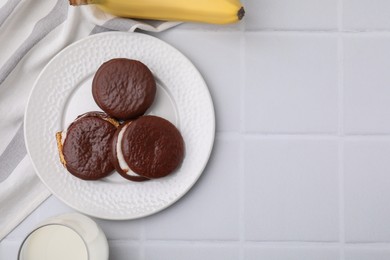 Photo of Tasty sweet choco pies, banana and glass on milk white tiled table, flat lay. Space for text