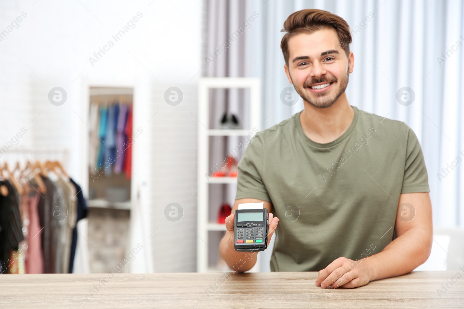 Photo of Male shop assistant with payment terminal at counter. Space for text