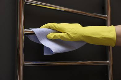 Photo of Woman cleaning heated towel rail with rag, closeup