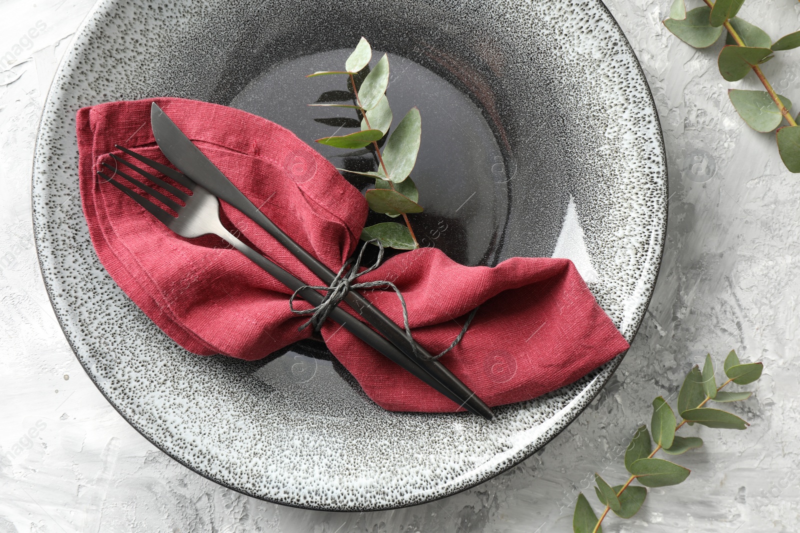 Photo of Stylish setting with cutlery, napkin, eucalyptus branches and plate on grey textured table, top view