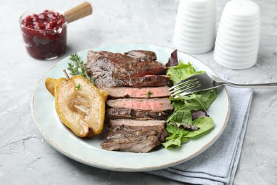 Delicious roasted beef meat, caramelized pear and greens served on light textured table