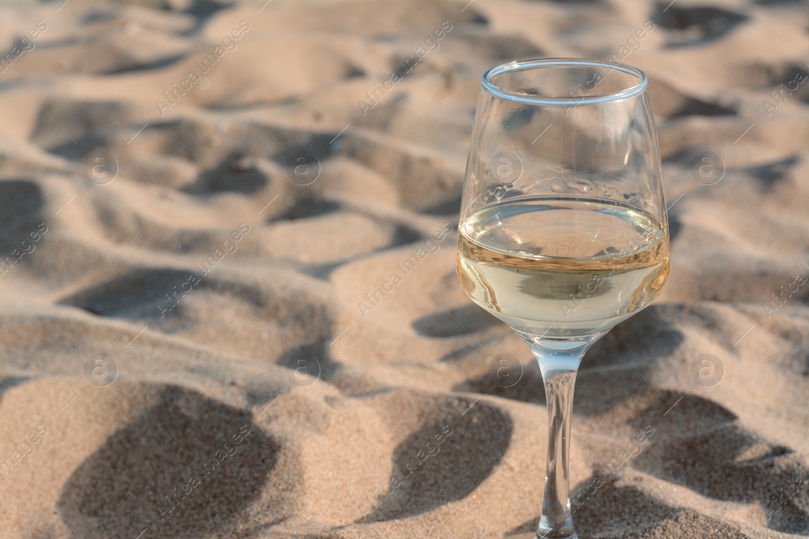 Photo of Glass of tasty wine on sand, space for text