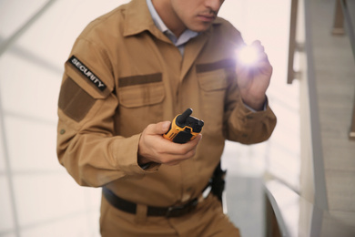 Photo of Professional security guard with portable radio set and flashlight indoors, closeup