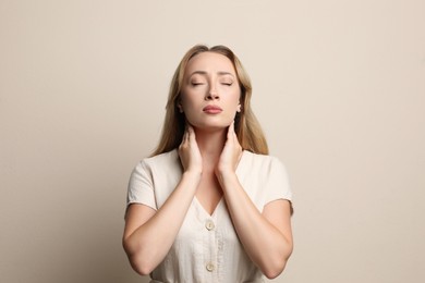 Photo of Young woman doing thyroid self examination on beige background