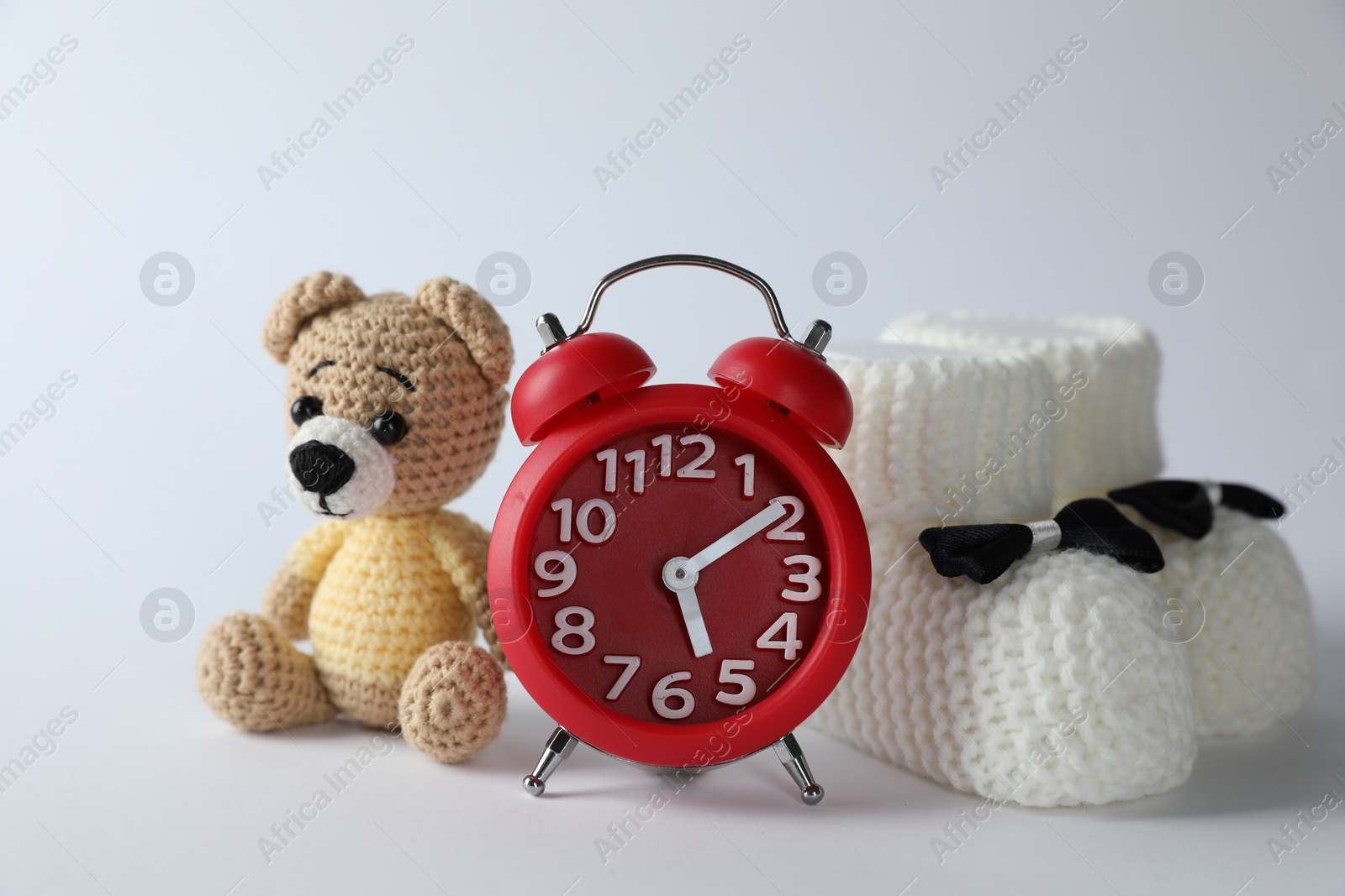 Photo of Alarm clock, toy bear and baby booties on white background. Time to give birth