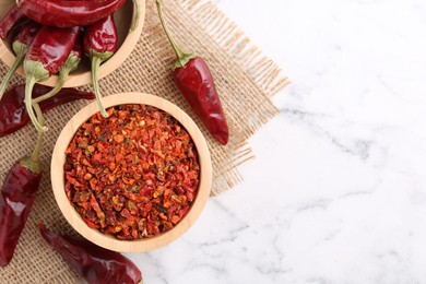 Photo of Chili pepper flakes and pods on white marble table, top view. Space for text