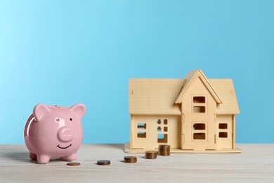 Piggy bank, little house model and stacks of coins on white wooden table