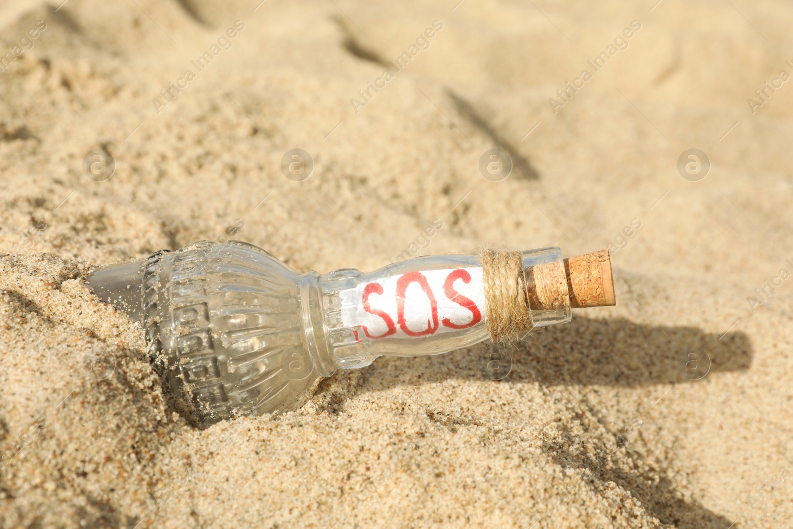 Photo of Glass bottle with SOS message on sand, closeup