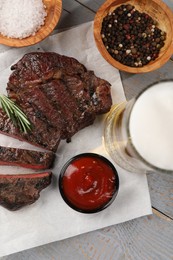 Mug with beer, fried steak and sauce on grey wooden table, flat lay